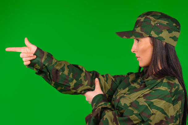 Portrait of a woman in military uniform, hands imitating weapons on green. Violation of gender stereotype. High quality photo - Foto, Imagem