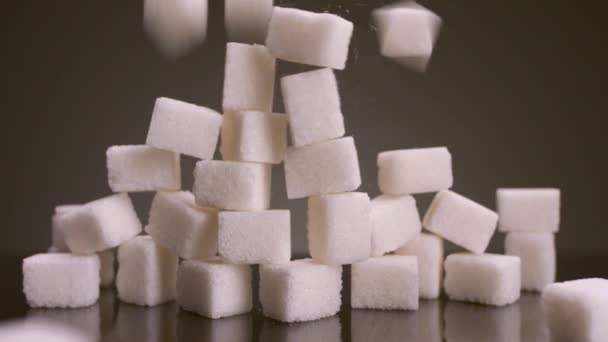 Zuckerwürfel auf isoliertem Hintergrund. Archivmaterial. Turm aus Zuckerwürfeln stürzt auf isoliertem Hintergrund ein. Süßigkeiten in großen Mengen sind gesundheitsschädlich. Zucker und Süßigkeiten sind die Sucht des 21. Jahrhunderts - Filmmaterial, Video