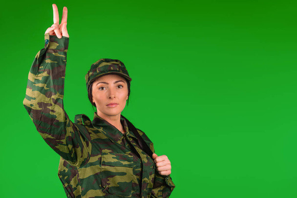Woman in military uniform showing the victory sign on green with blank space. Gender equality. High quality photo - Photo, image