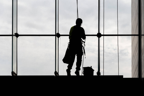 İşçi siluetleri, ekipman araçları kullanarak ön pencere camlarını temizliyor, yüksek risklerle çalışıyor. - Fotoğraf, Görsel