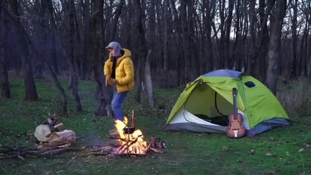 Grappige vent danst bij een tent en een kampvuur in het bos - Video