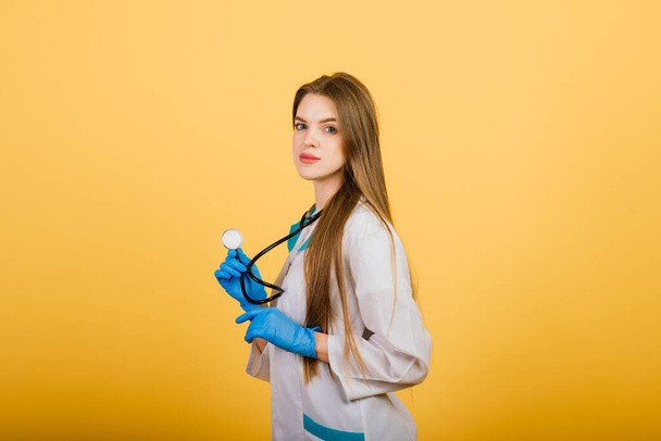 Retrato de mujer doctora con estetoscopio mirando a la cámara sobre fondo amarillo, atención médica - Foto, imagen