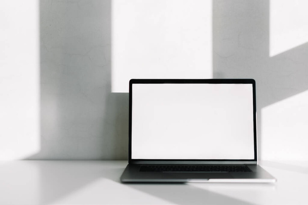 Laptop computer with white blank screen on the white table with shadow from window. High quality photo - Photo, image