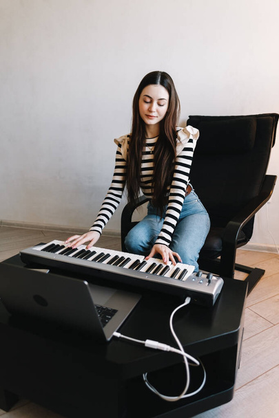 Молода жінка навчиться віддалено грати на клавішах піаніно, використовуючи ноутбук вдома
. - Фото, зображення
