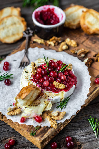 Traditional French homemade baked camembert with toasts, rosemary, cranberries and nuts on rustic wooden table. Gourmet traditional Breakfast. vertical image, top view. - Photo, Image