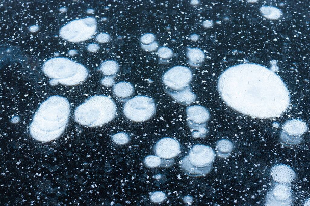 Abstraktní textura tmavého ledu s bílými kulatými skvrnami a sněhovými krystaly na povrchu. Zmrazení řeky - Fotografie, Obrázek