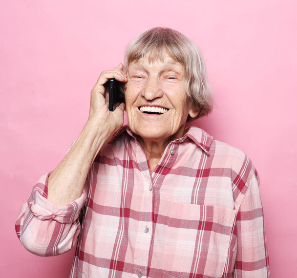 old woman wearing casual talking on cell phone over pink background - Zdjęcie, obraz