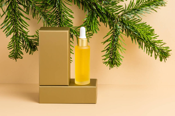 Yellow dropper bottle of serum or oil on golden podium with fir tree on neutral beige background. Organic skin care cosmetics with vitamin C, wellness, spa and beauty treatment concept, product mockup - Photo, Image