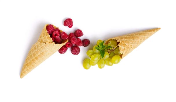 白い背景に隔離されたワッフルコーンの新鮮なラズベリーとブドウ。有機菜食、食料品の品揃え、天然物、健康的なライフスタイルの概念 - 写真・画像