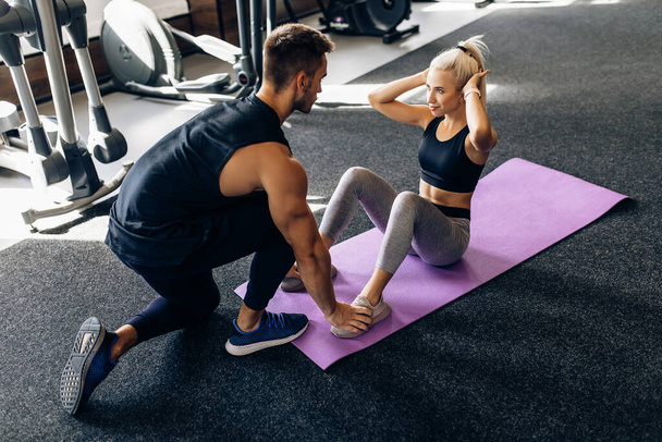 Sportive young woman doing abdominal exercises with a personal trainer lying on a fitness mat in the gym, fitness, sports, workout, - Foto, Imagen