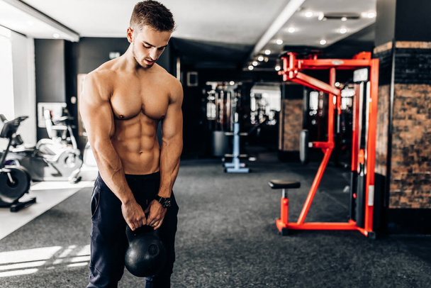 Fit muscular young man focused on lifting dumbbells while exercising in the gym - 写真・画像