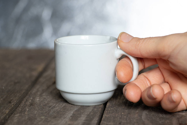 mano femenina sosteniendo una pequeña taza de café en una mesa de madera en un café - Foto, Imagen