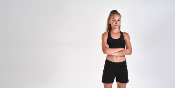 Portrait of cute sportive girl child in black sportswear looking at camera, standing with arms crossed while posing isolated over white background - Fotografie, Obrázek