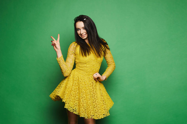 Beautiful and stylish model brunette girl in short yellow dress, with sunglasses on her head, smiling and have a fun at green background, isolated in studio - Φωτογραφία, εικόνα