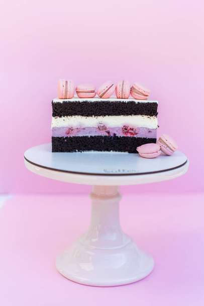 Gâteau éponge avec intercalaire crème sur fond rose isolé. Décoré avec des macarons roses - Photo, image