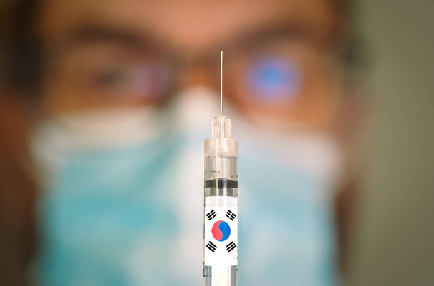 Detailní záběr injekční stříkačky s korejským a rozmazaným lékařem na pozadí. - Fotografie, Obrázek