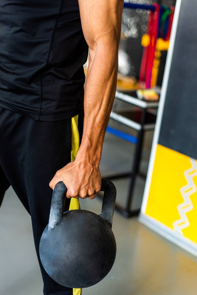 Young African American athlete trains in the gym with kettlebell weights. Black muscular man. Close-up of hands. In the background is the gym. Handsome black sports trainer. - Foto, Imagen