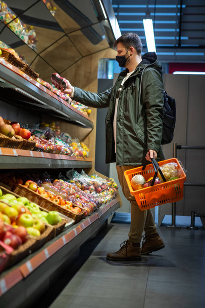 mężczyzna kupuje owoce w sklepie spożywczym mas medycznych na twarzy koncepcja covid-19 - Zdjęcie, obraz