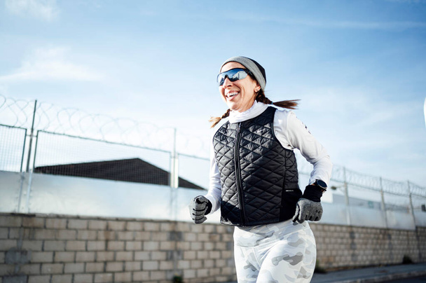 Sportvrouw loopt rond industriële zone in de winter, terwijl de zon opkomt. - Foto, afbeelding