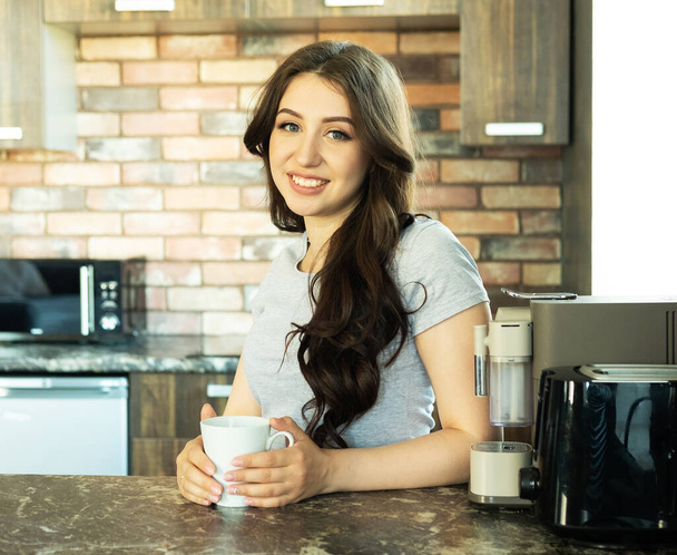 Beautiful young woman drinking coffee in kitchen - Фото, изображение
