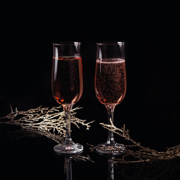 Two glasses of rose champagne and Christmas or New Year decoration on black background. Romantic dinner. Winter holiday concept. - Photo, Image