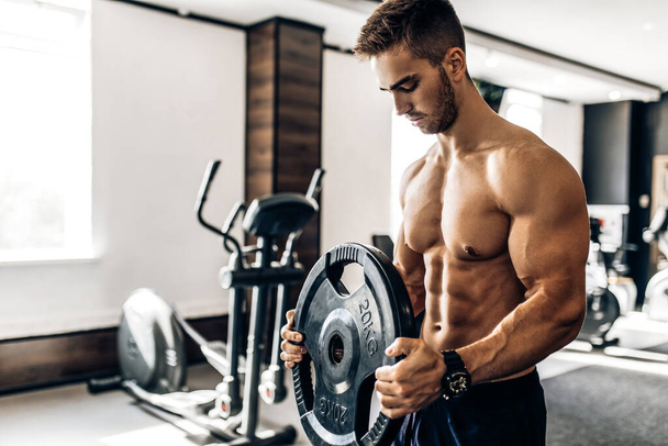 Muscular shirtless young man lifts weights exercising with dumbbells in the gym - Fotoğraf, Görsel