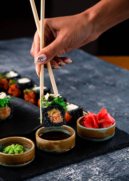 Sushi rolls set served on black stone slate on dark background, set of Japanese sushi rolls with soy sauce, ginger and wasabi - Foto, Imagen