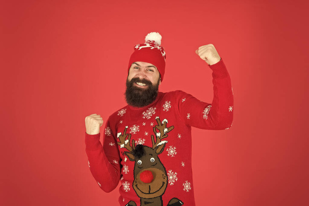 Christmas Deals start. mature hipster beard in knitted sweater. get warm in cold season. winter clothes fashion. festive holiday atmosphere. portrait of happy santa man. bearded man in hat red wall - Fotoğraf, Görsel