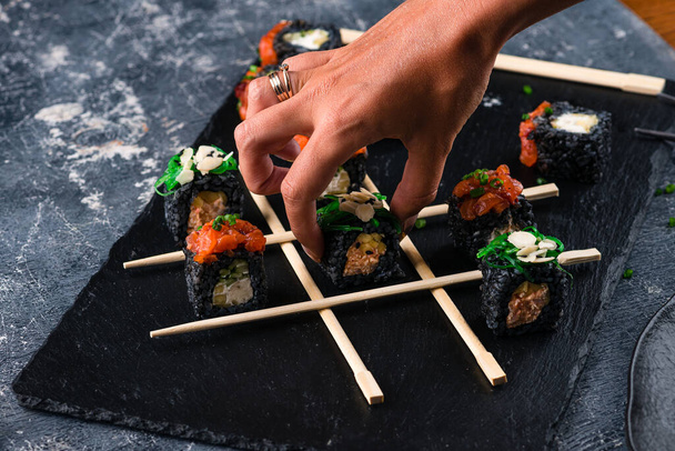 Japanese set sushi Maki rolls on a black slate with sticks like TIC TAC toe, tic tac toe sushi on dark background creative concept sushi - Valokuva, kuva