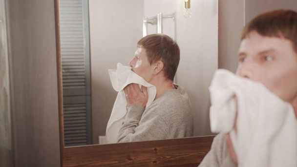 Aikuinen mies kylpyhuoneessa on harjannut hampaansa, pessyt ja pyyhkii kasvonsa ja kätensä kuivaksi valkoisella pyyhkeellä.. - Valokuva, kuva