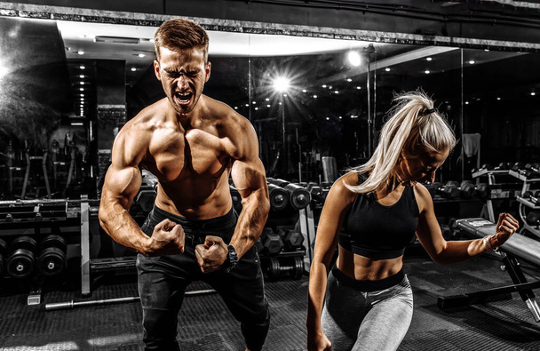 Excited screaming people, muscular man and woman, sportive couple standing in the gym, on black background - Fotoğraf, Görsel