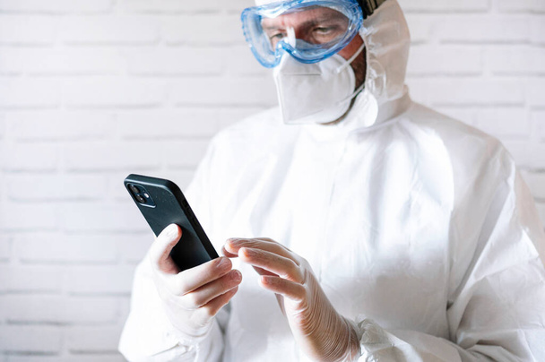 Медсестра в защитном костюме и смартфоне - Фото, изображение