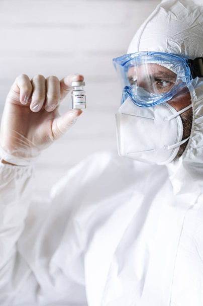 Чоловіча медсестра в захисному костюмі показує вакцину COVID 19 на камеру
 - Фото, зображення