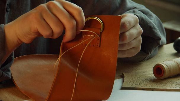 Gros plan sur le processus de couture de la fixation de la poignée d'un sac en cuir. Les mains du tailleur mettent le fil dans les trous. - Photo, image