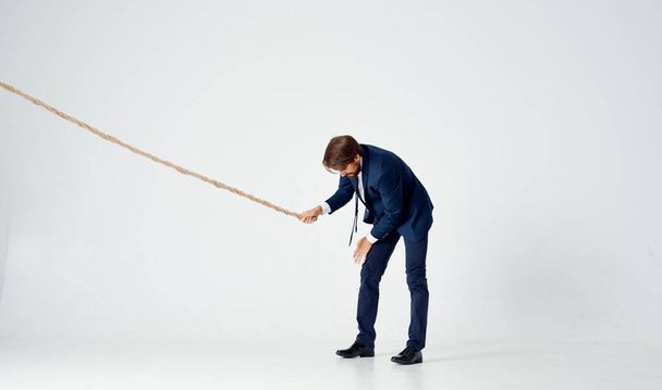 a business man lies on the floor and pulls a rope on a light background indoors - Photo, Image