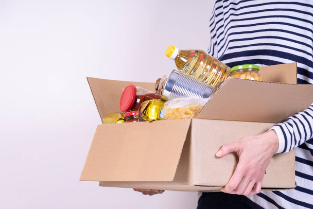 Wolontariusze trzymają na białym biurku pudełko z darowiznami żywnościowymi z produktami spożywczymi - Zdjęcie, obraz