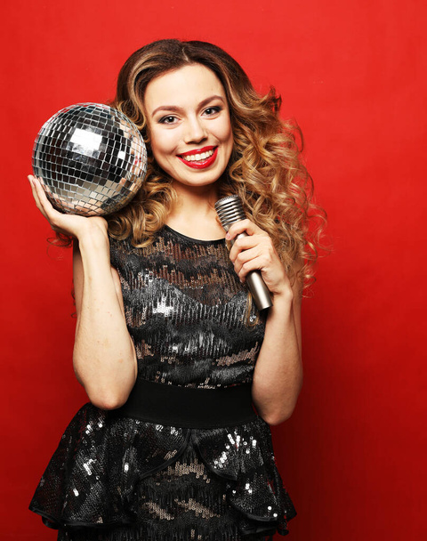 Young blond woman with long wavy hair dressed in evening dress holding a microphone and disco ball, - Foto, afbeelding
