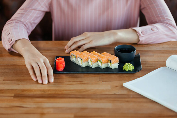female hands on the table in front of a dish with sushi and a magazine - Foto, Bild