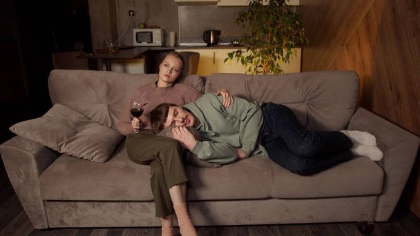 居心地の良いスタジオアパートメントの若いカップルは、テレビの前の夜にリラックスしています。夫はシリーズを見ながら妻の膝の上で眠りに落ちた。彼女は彼を優しく抱きしめる. - 写真・画像