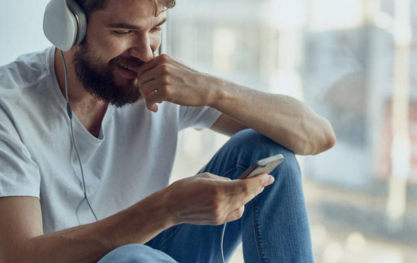 veselý muž ve sluchátkách poslouchá hudbu na parapetu - Fotografie, Obrázek