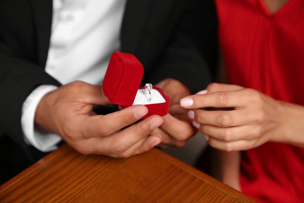 Man with engagement ring making proposal to his girlfriend at table, closeup - Foto, imagen