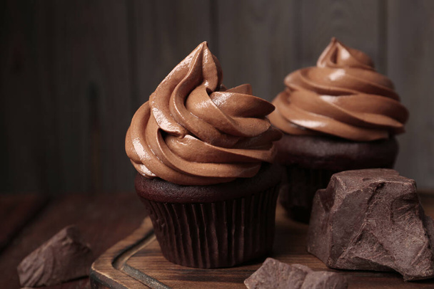 Delicious cupcakes with cream and chocolate pieces on wooden table, closeup - Photo, image