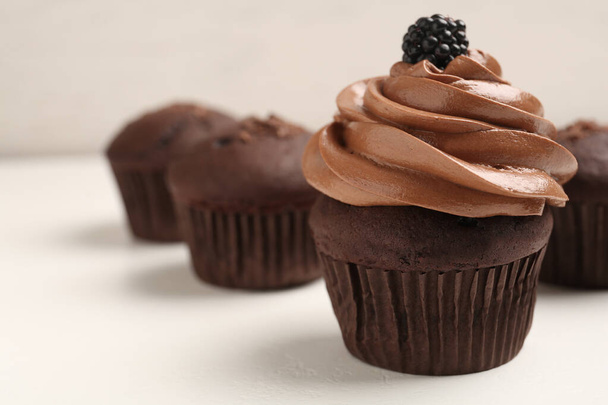Delicious chocolate cupcake with cream and blackberry on white table, closeup. Space for text - Photo, image