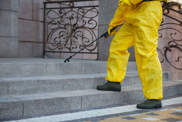 Person in hazmat suit disinfecting stairs with sprayer outdoors, closeup. Surface treatment during coronavirus pandemic - Фото, зображення