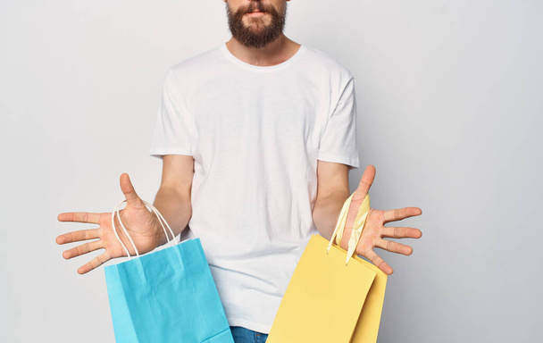 Sokszínű csomagok egy férfi fehér póló bevásárló stúdió kezében - Fotó, kép