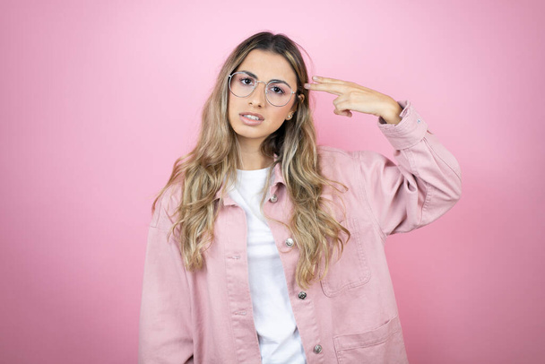 Young beautiful blonde woman with long hair standing over pink background Shooting and killing oneself pointing hand and fingers to head like gun, suicide gesture. - Photo, Image