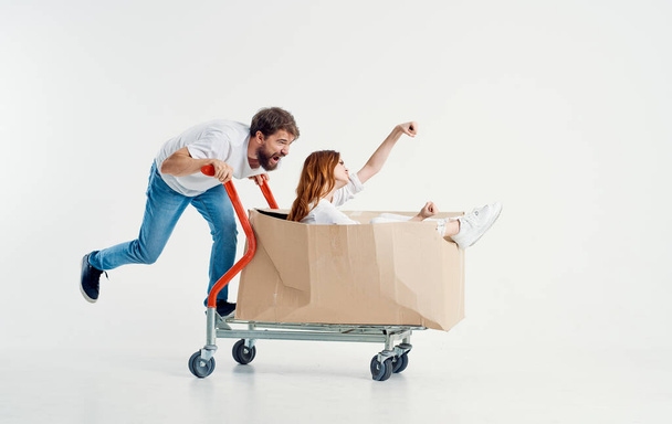 cheerful woman in a box on a cargo trolley and energetic courier in jeans and a t-shirt - Foto, immagini