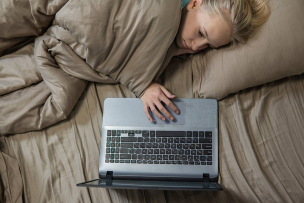 Teenage girl lies in bed and works on laptop. high quality - 写真・画像