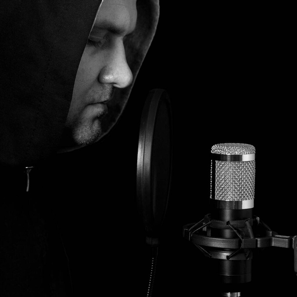 De zanger-artiest staat aan de microfoon. Een kunstenaar met zijn ogen dicht aan de microfoon. Een nieuw nummer opnemen. Opnamestudio - Foto, afbeelding