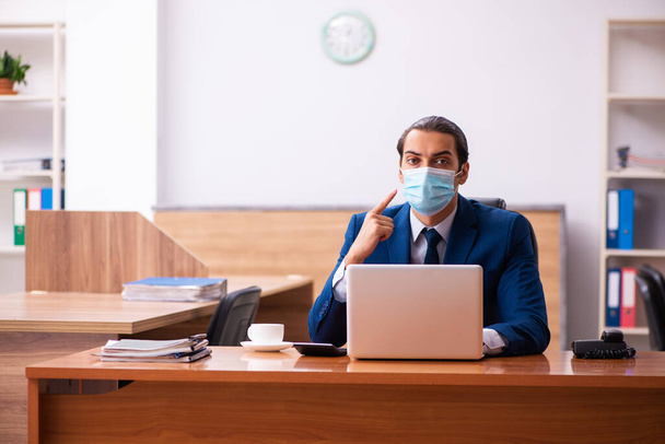 Jeune employé masculin travaillant dans le bureau portant un masque - Photo, image